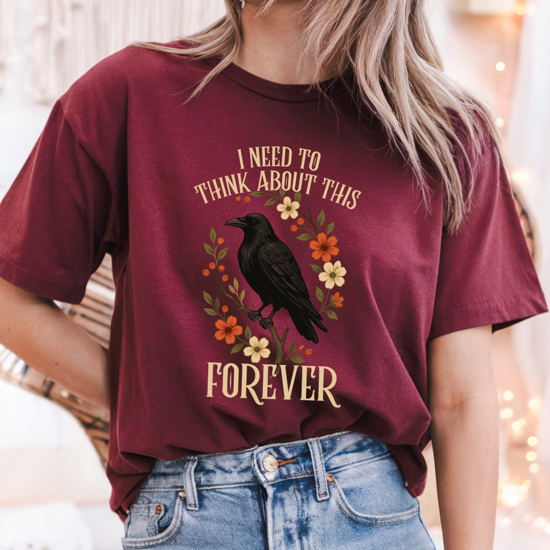 A woman wearing a maroon graphic t-shirt with a black raven and floral design, paired with light blue jeans.