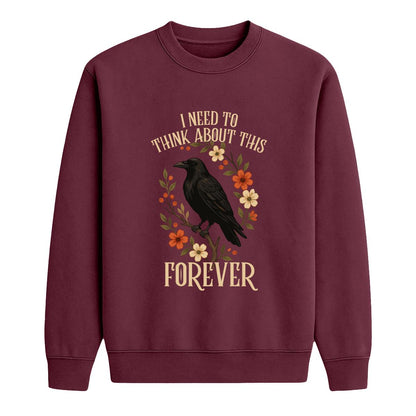 A maroon crewneck sweatshirt featuring a graphic of a black raven surrounded by orange, yellow, and cream flowers, with the text 'I NEED TO THINK ABOUT THIS FOREVER' in a cream-colored font.