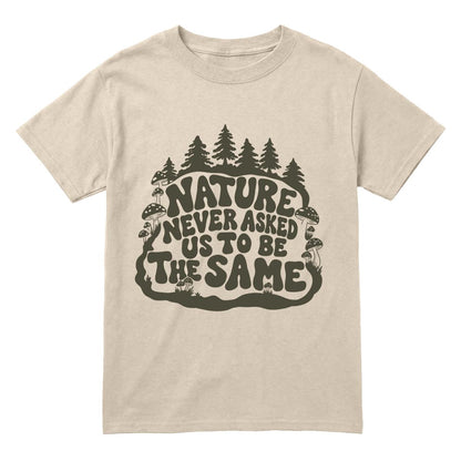 A sand crewneck t-shirt with a dark olive green graphic on the front featuring pine trees and the text 'NATURE NEVER ASKED US TO BE THE SAME'.