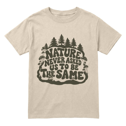 A sand crewneck t-shirt with a dark olive green graphic on the front featuring pine trees and the text 'NATURE NEVER ASKED US TO BE THE SAME'.