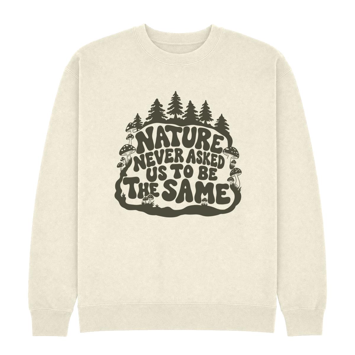 An off-white crewneck sweatshirt featuring a dark olive green graphic on the chest with the text 'NATURE NEVER ASKED US TO BE THE SAME' surrounded by pine trees, mushrooms, and a snake.