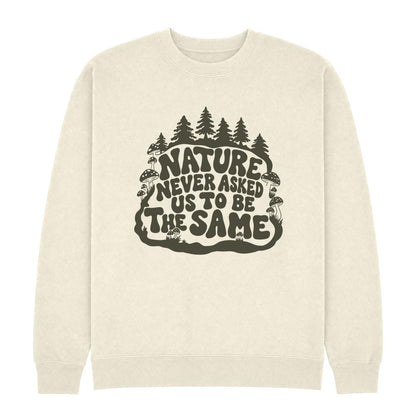 An off-white crewneck sweatshirt featuring a dark olive green graphic on the chest with the text 'NATURE NEVER ASKED US TO BE THE SAME' surrounded by pine trees, mushrooms, and a snake.