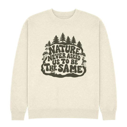 An off-white crewneck sweatshirt featuring a dark olive green graphic on the chest with the text 'NATURE NEVER ASKED US TO BE THE SAME' surrounded by pine trees, mushrooms, and a snake.