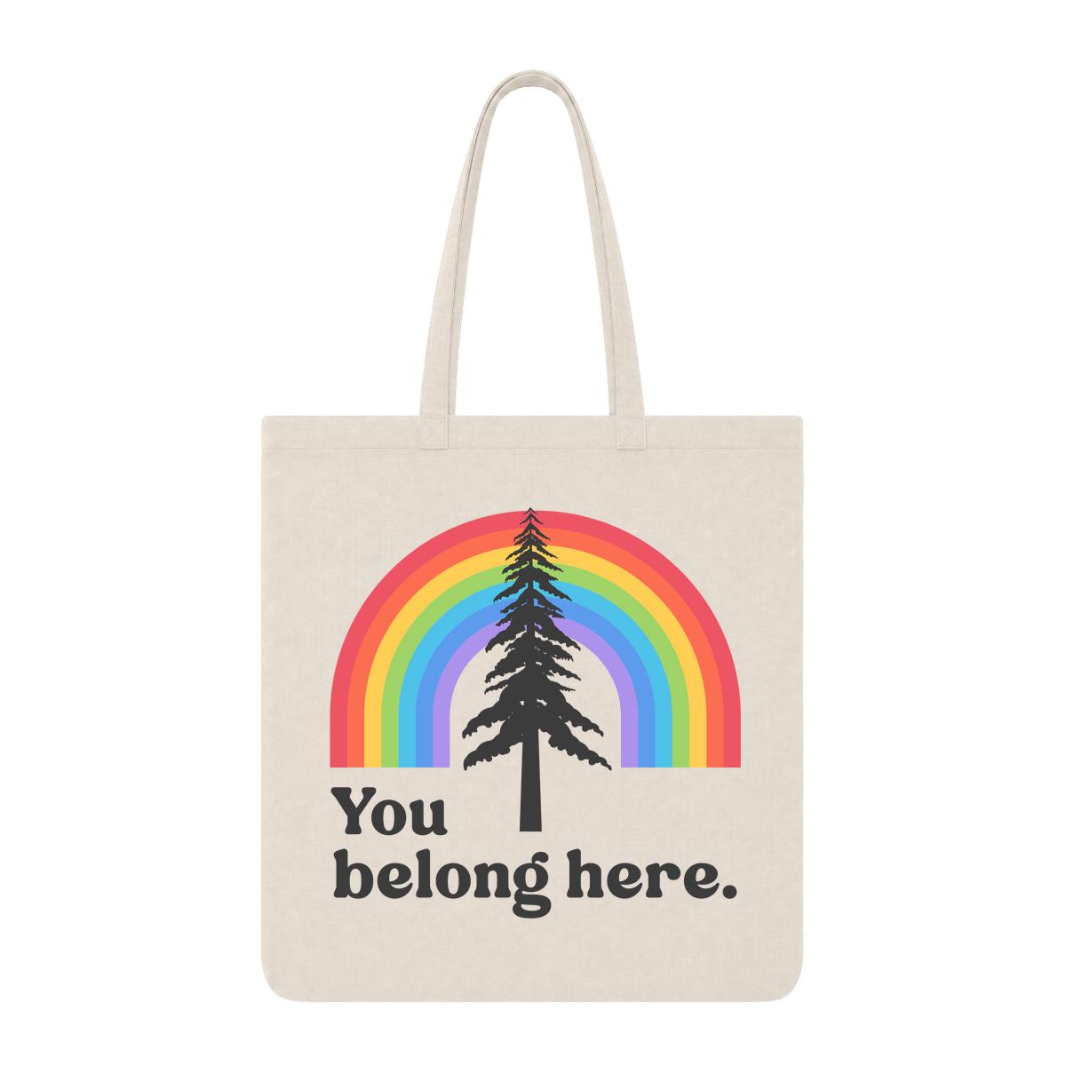 Natural tote bag with rainbow and pine tree graphic and “You Belong Here” text